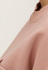 Dammrosa sweatshirt med ribbad halsringning och mjukt, texturerat tyg. Har en avslappnad passform och minimalistiska design detaljer.