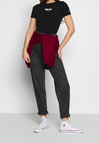 Černé tričko s krátkým rukávem s logem "Tommy Jeans", doplněné volnými šedými džínami a bílými vysokými teniskami. Červený svetr uvázaný v pase.