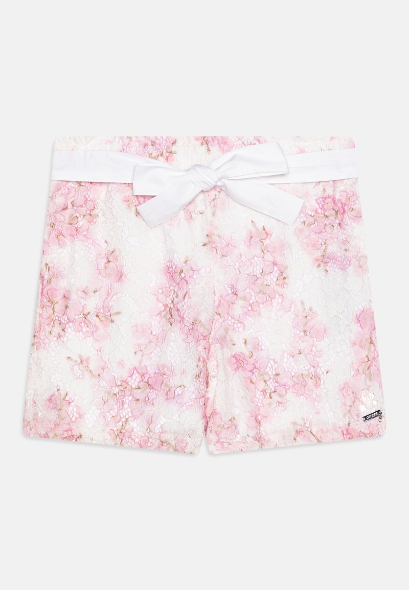 Shorts blancs avec superposition en dentelle florale rose, dotés d'un grand nœud en tissu blanc noué à la taille et d'une petite étiquette de marque à l'ourlet.