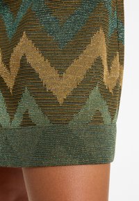 Knit skirt featuring a chevron pattern in shades of green, gold, and brown with a textured finish and a solid green hem.