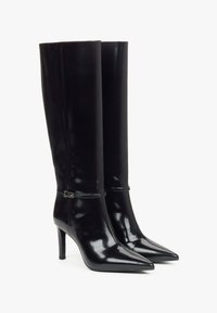 Černé vysoké kozačky na podpatku vyrobené z lesklé lakované kůže, se špičatou špičkou, designem až ke kolenům a jemným akcentem v oblasti kotníku v podobě přezky.