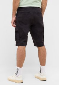 Czarne szorty cargo z bocznymi kieszeniami, luźnym krojem i gładką fakturą. Noszone z białymi trampkami i wzorzystymi skarpetkami.