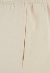 Beige joggerit, joissa on pehmeä, tekstuurinen kangas. Niissä on joustava vyötärönauha ja sivutaskut, mikä korostaa rentoa muotoilua.
