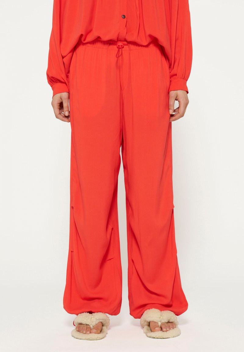 Rode wijde broek van lichtgewicht stof, met een elastische tailleband met trekkoord en zijzakken; gecombineerd met pluche slippers.