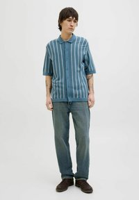 Polo en tricot bleu avec des rayures verticales, manches courtes et fermeture à boutons, associé à un jean en denim bleu ample et des chaussures marron.