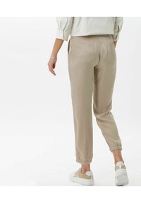 Beżowe lniane spodnie z elastycznymi mankietami, dwiema tylnymi kieszeniami i luźnym krojem, noszone z białymi i beżowymi trampkami.