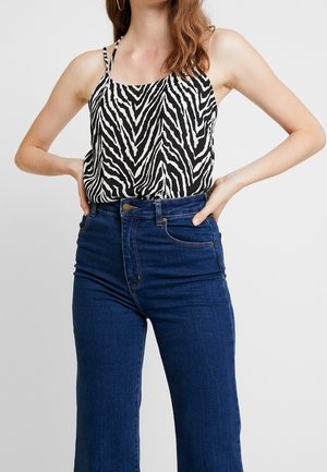 Camiseta de tirantes fina con estampado de cebra en blanco y negro, combinada con unos pantalones vaqueros acampanados de tiro alto en azul oscuro, que cuentan con bolsillos clásicos y costuras.