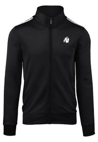 Zwarte sportjack met ritssluiting, gemaakt van glanzende stof. Voorzien van een hoge kraag, twee zijzakken en een wit logo op de borst en schouders.