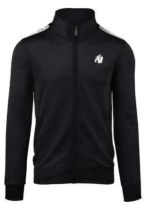 Zwarte sportjack met ritssluiting, gemaakt van glanzende stof. Voorzien van een hoge kraag, twee zijzakken en een wit logo op de borst en schouders.