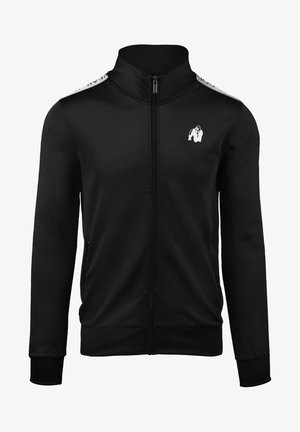 Zwarte sportjack met ritssluiting, gemaakt van glanzende stof. Voorzien van een hoge kraag, twee zijzakken en een wit logo op de borst en schouders.