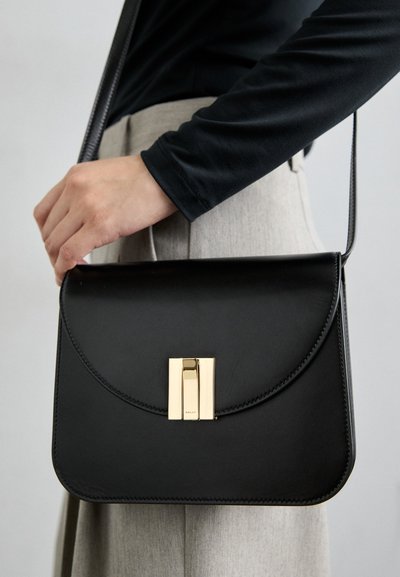 Black leather shoulder bag with a gold clasp, curved flap design, and contrasting stitching. The strap is slender and adjustable.