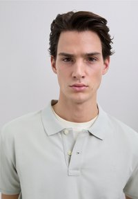 Lichtgrijs poloshirt van gestructureerde katoen, met een kraag, drieknopenhals en een klein logo op de linkerborst.