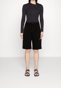 Mustat farkkushortsit, joissa on etunapitus, sivutaskut ja rento istuvuus, yhdistetty tumman pitkähihnaisen paidan ja mustien sandaalien kanssa.