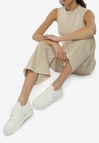 Hvide snørebåndssneakers med mesh og tekstureret gummisål, parret med beige cropped bukser og en ærmeløs beige top.