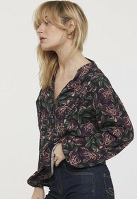 Chemise boutonnière florale en violet foncé avec des motifs de pivoine verts et roses, dotée d'un col et de manches longues à coupe décontractée.