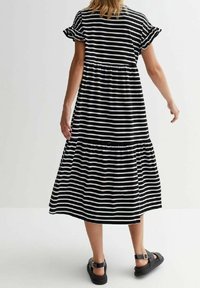 Mustat ja valkoiset raidalliset maksimekot, joissa on lyhyet, röyhelöillä varustetut hihat, kerätty vyötärö ja suorastaan virtaava hameosa. Yhdistetty mustiin sandaaleihin.