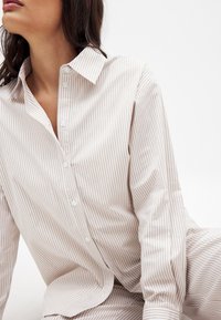 Button-up shirt in light beige with narrow vertical stripes. Made of smooth fabric, featuring a pointed collar and long sleeves.