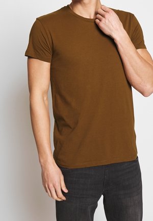 Camiseta de algodón marrón con cuello redondo y mangas cortas. La tela es suave, ajustada y presenta un sutil estiramiento.