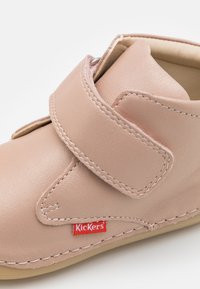 Rózsaszín bőrcipő, tépőzárral, lekerekített formájú, bézs talppal és piros Kickers címkével az oldalon. Simán tapintású és minimalista dizájn.