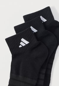 Čierne ponožky zo zmesi bavlny s rebrovanými manžetami, vybavené bielym logom Adidas a textúrovanými pruhmi na tele. Tri páry na sebe.
