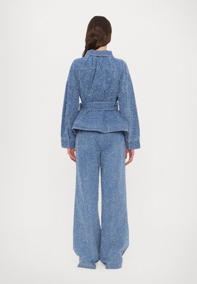 Conjunt de jachetă și pantaloni din denim de culoare albastru deschis, cu o textură speckled. Jacheta are o talie cu curea și mâneci supradimensionate.