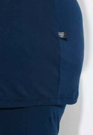 Gros plan sur l'ourlet d'un vêtement bleu marine avec une étiquette de marque visible cousue dans la couture latérale du tissu.