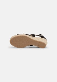 Sandale compensée noire avec détail en jute tressé, bride ajustable, semelle extérieure en caoutchouc texturé et matériau supérieur lisse.
