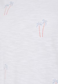 Tissu blanc à manches courtes avec une apparence texturée, présentant de petits motifs de palmiers bleus et des tiges rouges subtiles dispersées sur la surface.