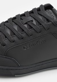 Baskets en cuir noir avec dessus texturé, lacets plats noirs et marquage embossé. Semelle en caoutchouc avec motif de crampons texturé.