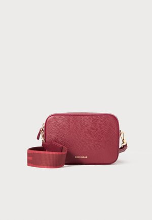 Burgundy leather crossbody bag with a rectangular shape, textured finish, gold hardware, and a adjustable fabric strap featuring stripes.