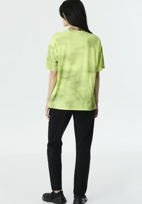 Camiseta de rayas de tie-dye verde con un corte relajado, mangas cortas y cuello redondo. Combinada con pantalones negros de cintura alta y zapatos negros.
