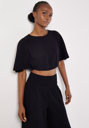 Zwart cropped top met korte mouwen en een gestructureerde afwerking, gecombineerd met hoge, lose zwarte broeken, beide in lichtgewicht stof.