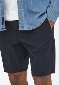 Marineblaue Baumwollshorts mit seitlichen Taschen, geradem Saum und glatter Textur, kombiniert mit einem hellen Jeanshemd.