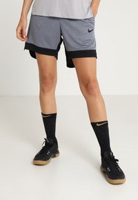 Šedé sportovní šortky s černým lemováním a texturovaným vzorem, doplněné černými ponožkami a černými sportovními botami. Viditelné logo Nike.