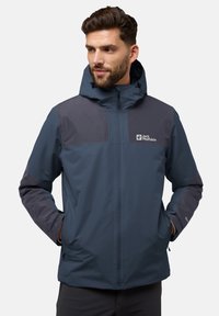 Veste imperméable bleu marine avec capuche, panneaux gris foncé contrastants, fermeture frontale zippée et logos sur la poitrine et la manche.