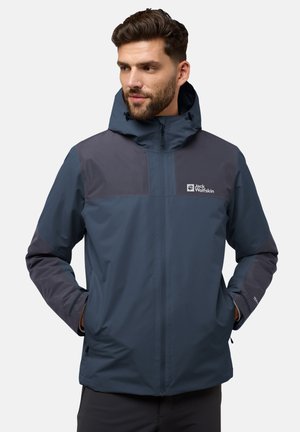 Giacca impermeabile blu navy con cappuccio, pannelli grigio scuro a contrasto, chiusura frontale con zip e loghi sul petto e sulla manica.