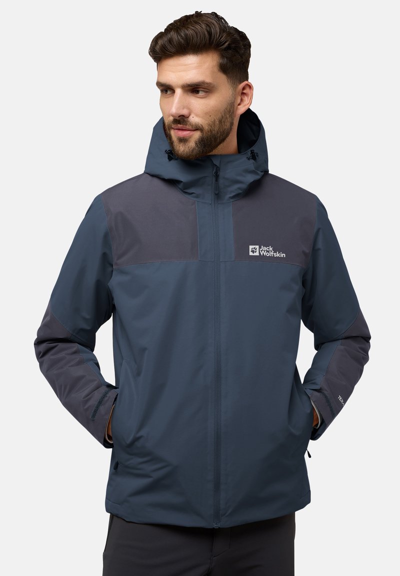 Veste imperméable bleu marine avec capuche, panneaux gris foncé contrastants, fermeture frontale zippée et logos sur la poitrine et la manche.