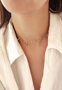 Collier choker en or avec des charms alternés de lune et d'étoile sur une chaîne torsadée, porté contre un tissu de couleur claire.