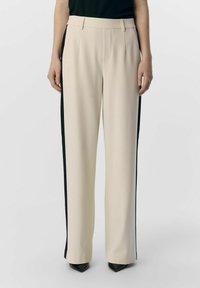 Pantaloni color crema con pannelli laterali neri, realizzati in tessuto liscio. Presentano un design a gamba dritta e una vita con passanti per cintura.