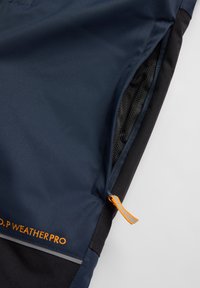 Marine-blauwe weersbestendige broek met een ritszak met een oranje trekband, zwarte accenten en reflecterende details langs de zijkanten.