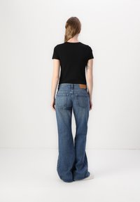 T-shirt noir à manches courtes associé à un jean flare bleu clair avec une patch en cuir à l'arrière et un design de poche simple.