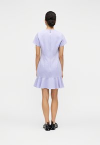 Λιλά φόρεμα με κοντά μανίκια και φουσκωτή γραμμή στο τελείωμα. Διαθέτει διακριτική λάμψη, φερμουάρ στο πίσω μέρος και διακοσμητικό κουμπί στο ντεκολτέ.