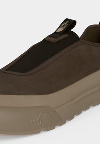 Καφέ sneaker slip-on με μαύρο ελαστικό πάνω μέρος και μπεζ σόλα με ανάγλυφο το λογότυπο The North Face στο πλάι.
