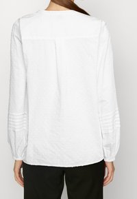 Blusa bianca con maniche lunghe, realizzata in un tessuto testurizzato con piccole punte sollevate, maniche arricciate e vestibilità comoda. Sul retro presenta un orlo dritto.