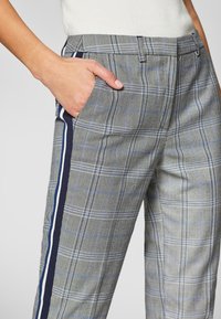 Grijze geruite broek met een gestructureerde stof, zijzakken en contrasterende marineblauwe strepen langs de buitennaden.