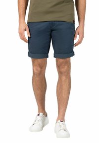 Marineblaue Baumwollshorts mit umgeschlagenen Säumen, kombiniert mit weißen Sneakers. Die Shorts verfügen über einen Reißverschluss und seitliche Taschen.