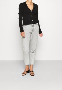 Černý žebrovaný kardigan s véčkovým výstřihem a pěti knoflíky, doplněný o světle šedé riflové kalhoty s vysokým pasem a černé sandály na podpatku.