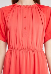 Robe midi corail en tissu léger, dotée d'un col rond avec volant élastique, de manches courtes, d'une fermeture à boutons sur le devant et d'une taille élastique.