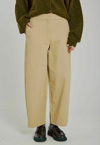 Beige vida byxor med en slät bomullstextur, med platt framdel och sidofickor. I kombination med mörka läderskor.