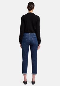 Donkerblauwe denim jeans met een rechte snit, opgerolde broekspijpen en twee achterzakken, gecombineerd met een zwart longsleeve shirt.